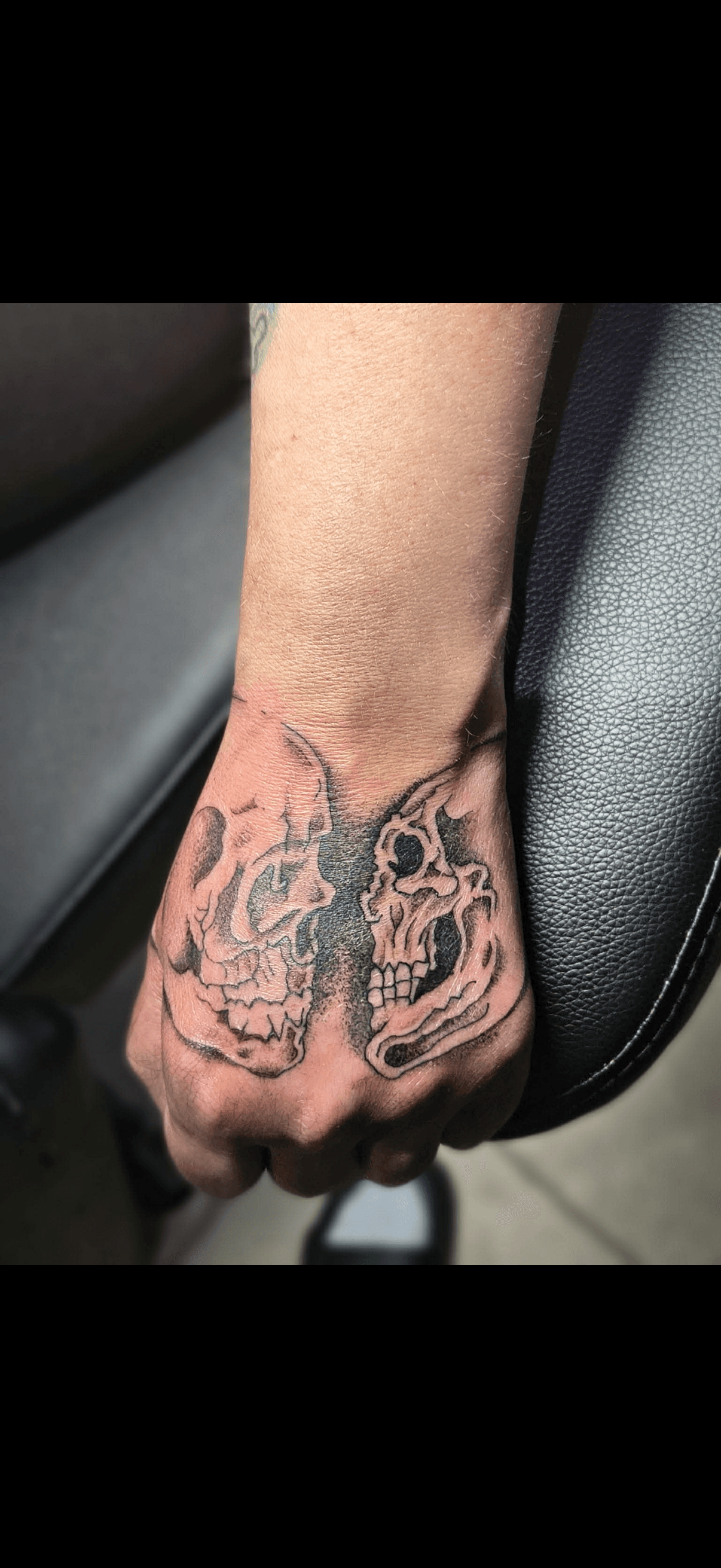 Black and grey hand tattoo of two skulls facing each other, forming a butterfly-like silhouette.