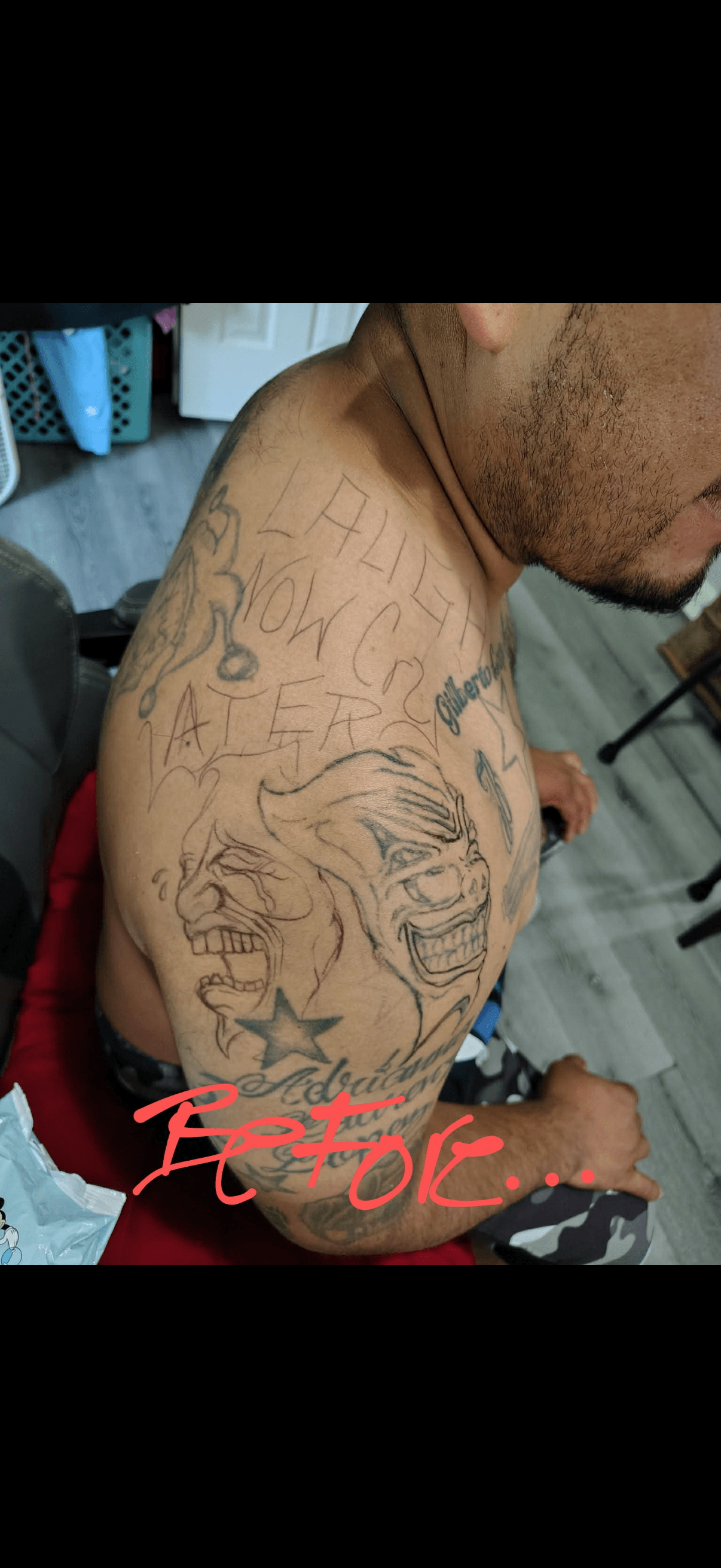 Man's upper arm featuring tattoos of comedy and tragedy masks and "Laugh Now Cry Later" text.