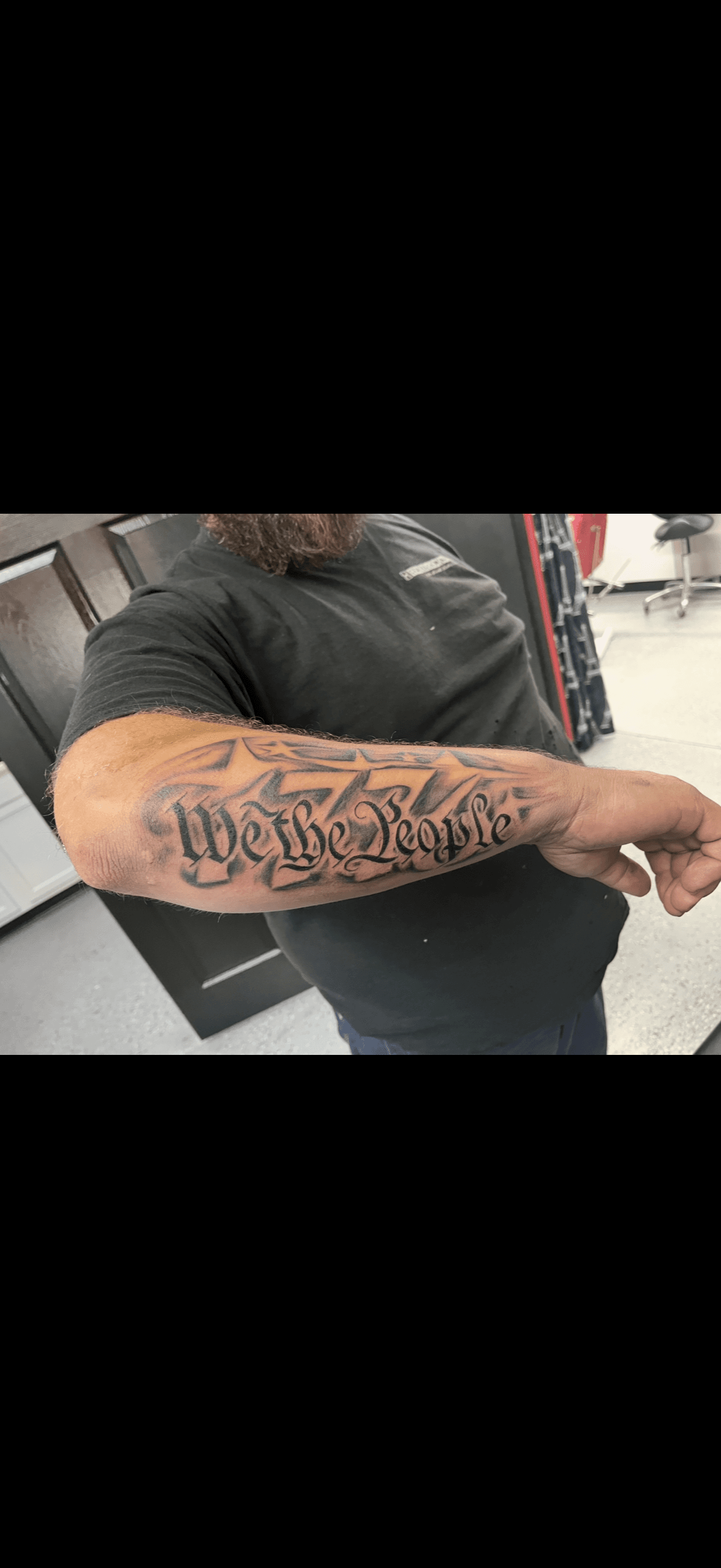 Black and grey forearm tattoo of 'We the People' in gothic script with stylized stars.