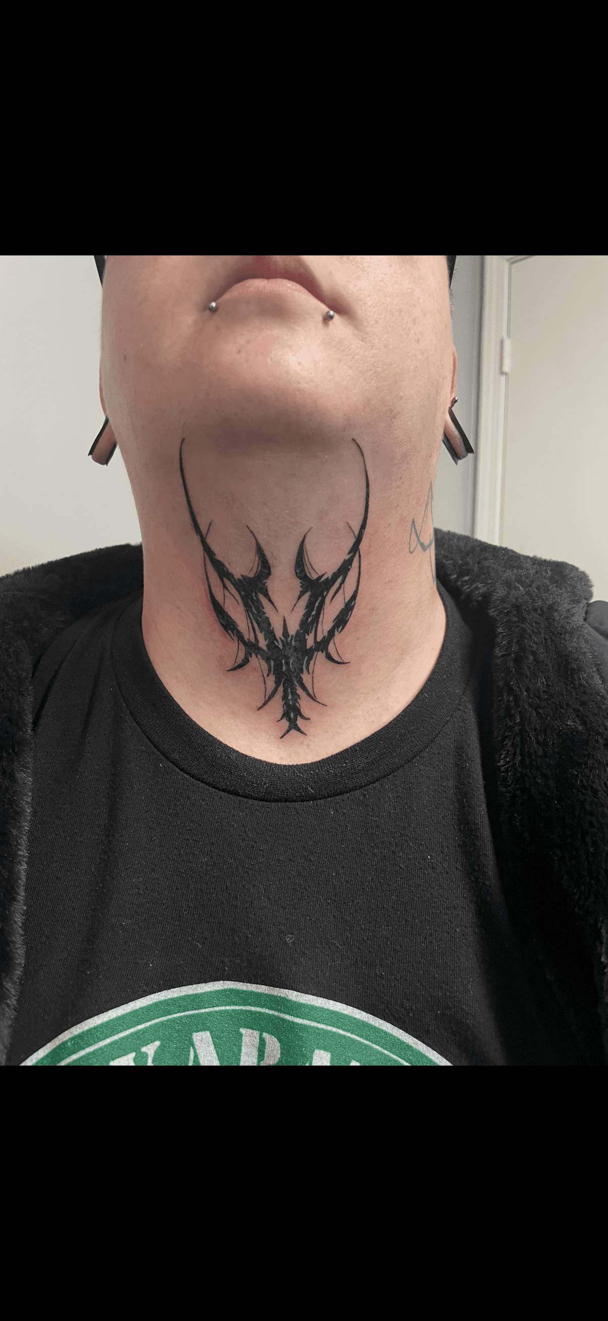 Symmetrical black tattoo with sharp, jagged lines on the front of a person's neck.