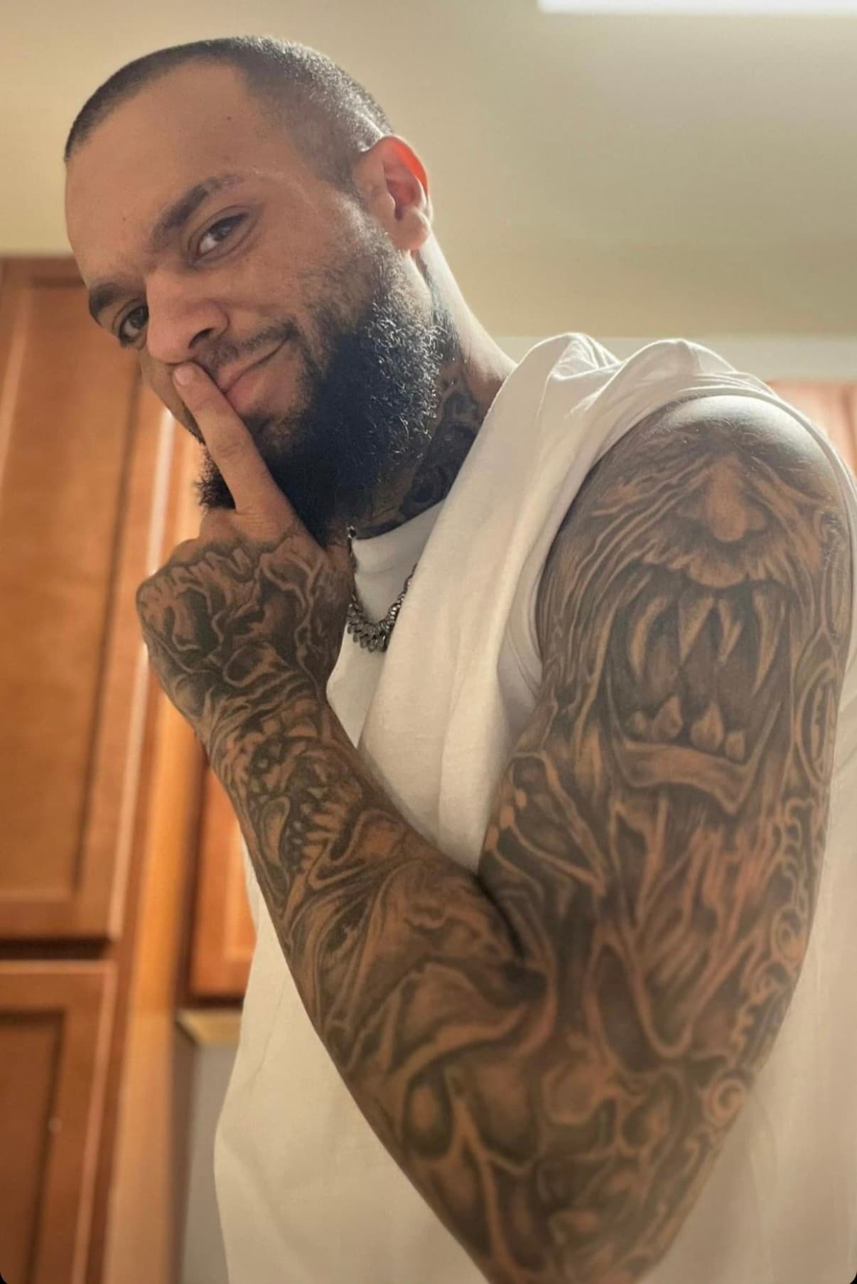 Bearded man with detailed arm tattoos makes a shushing gesture with his finger.