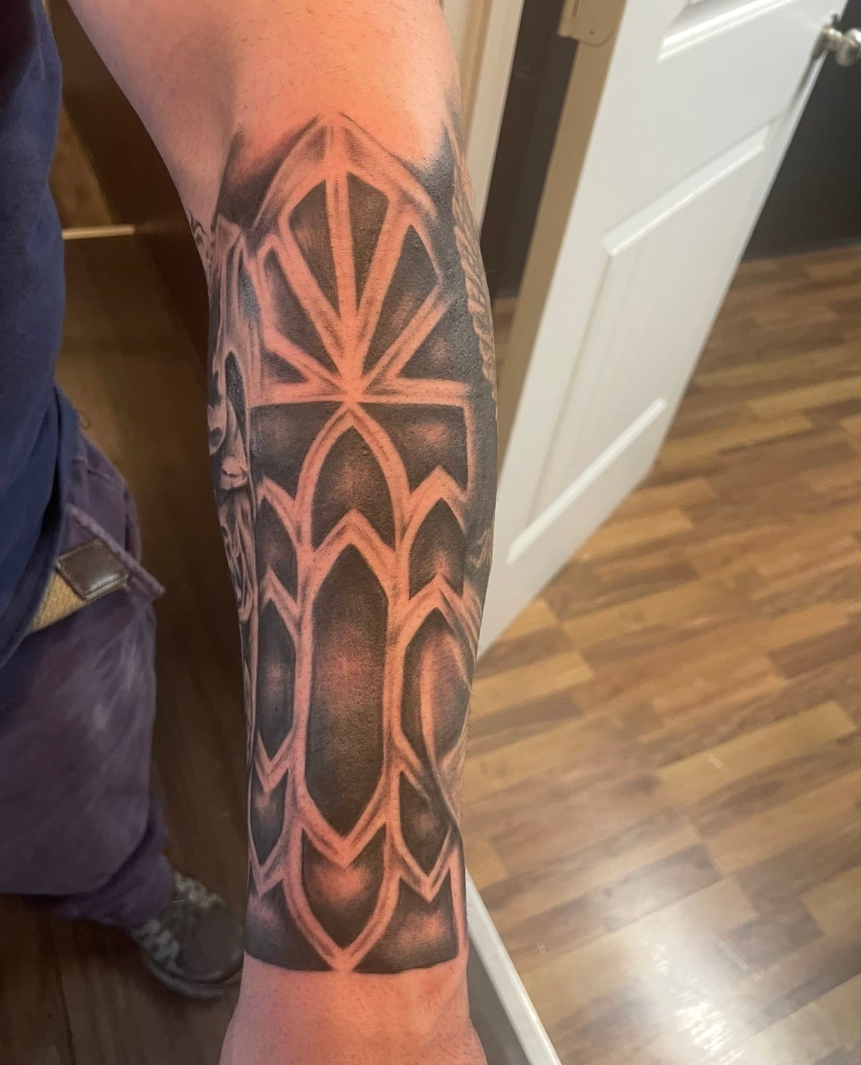 Intricate black and grey forearm tattoo showcasing geometric patterns resembling gothic cathedral window arches.