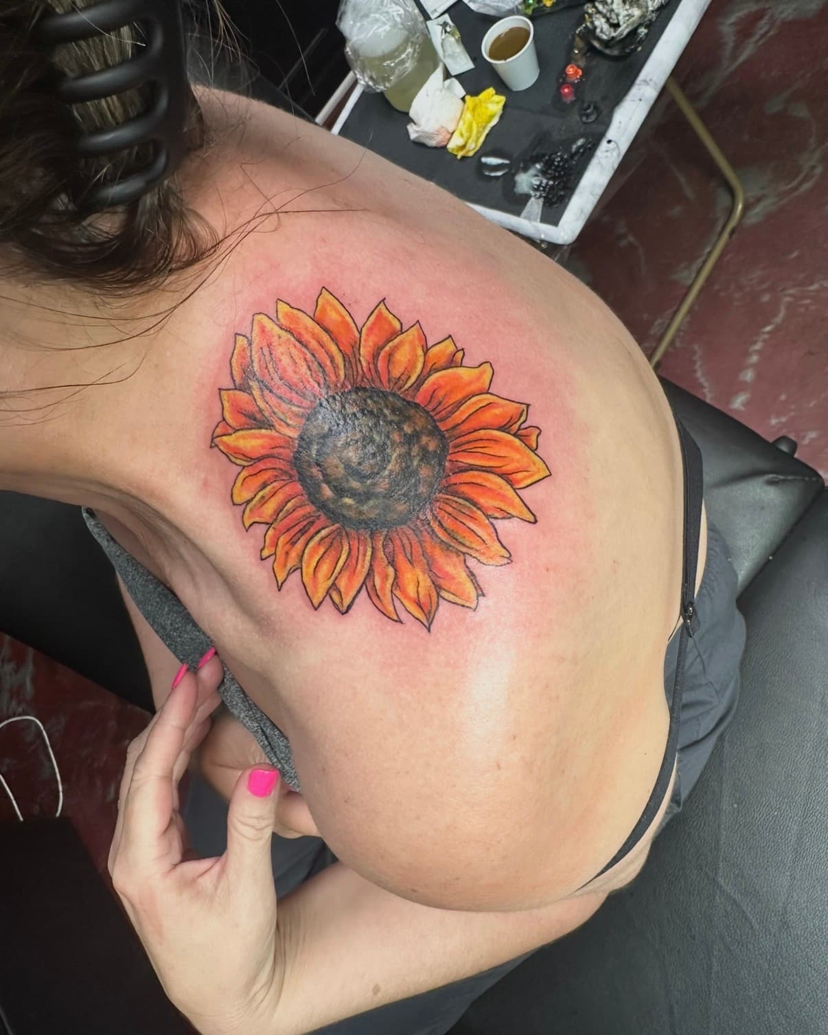Vibrant orange and yellow sunflower tattoo on a person's upper back and shoulder area.