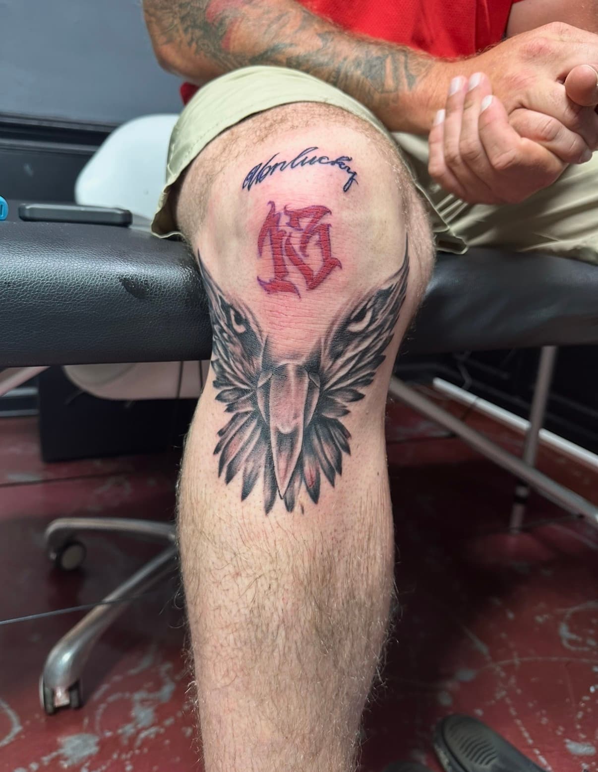 Man's knee tattoo with the word unlucky, a red thirteen, and a black eagle.