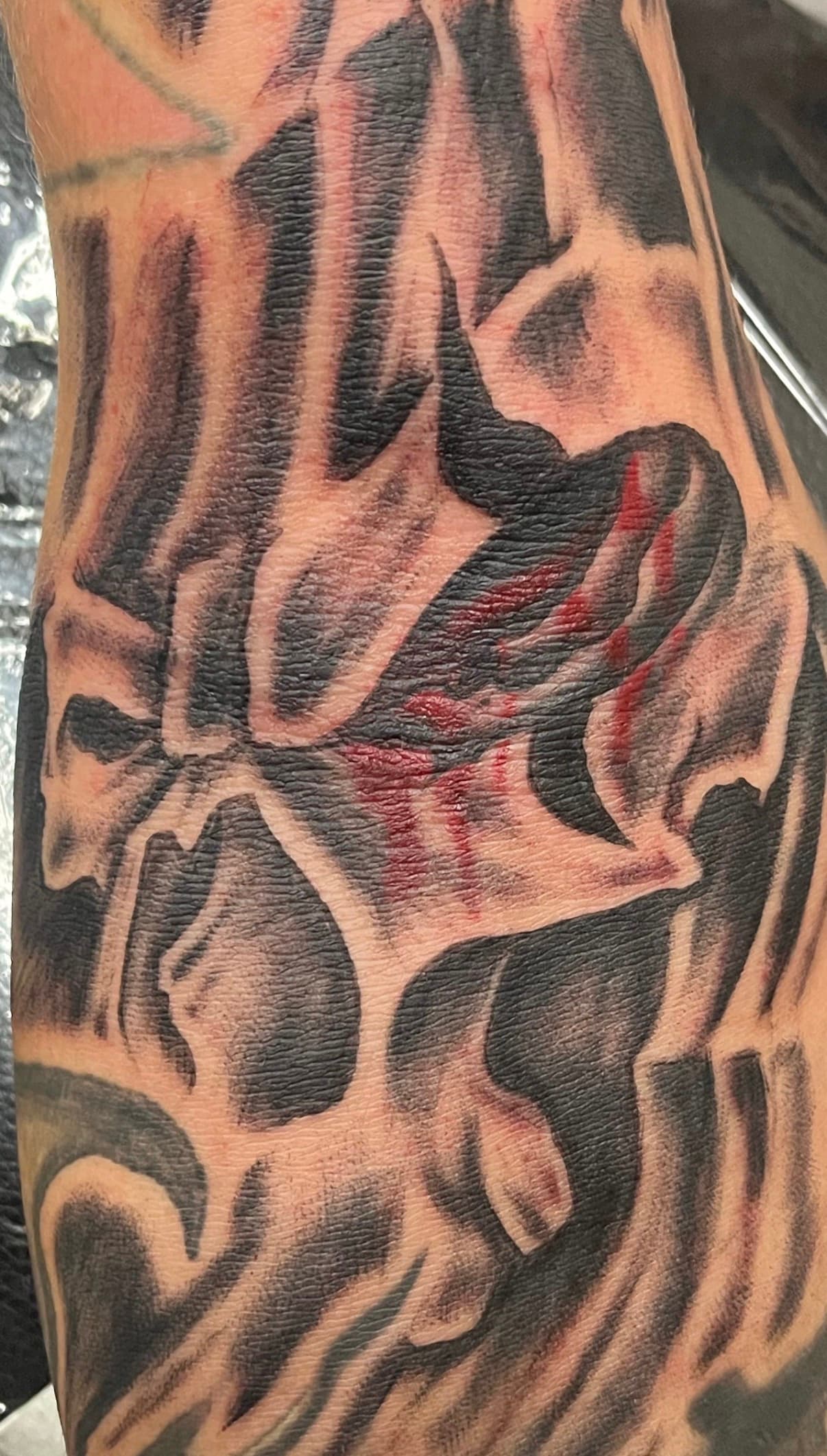 Close-up of a black abstract tattoo on skin with red spots and textured shading.