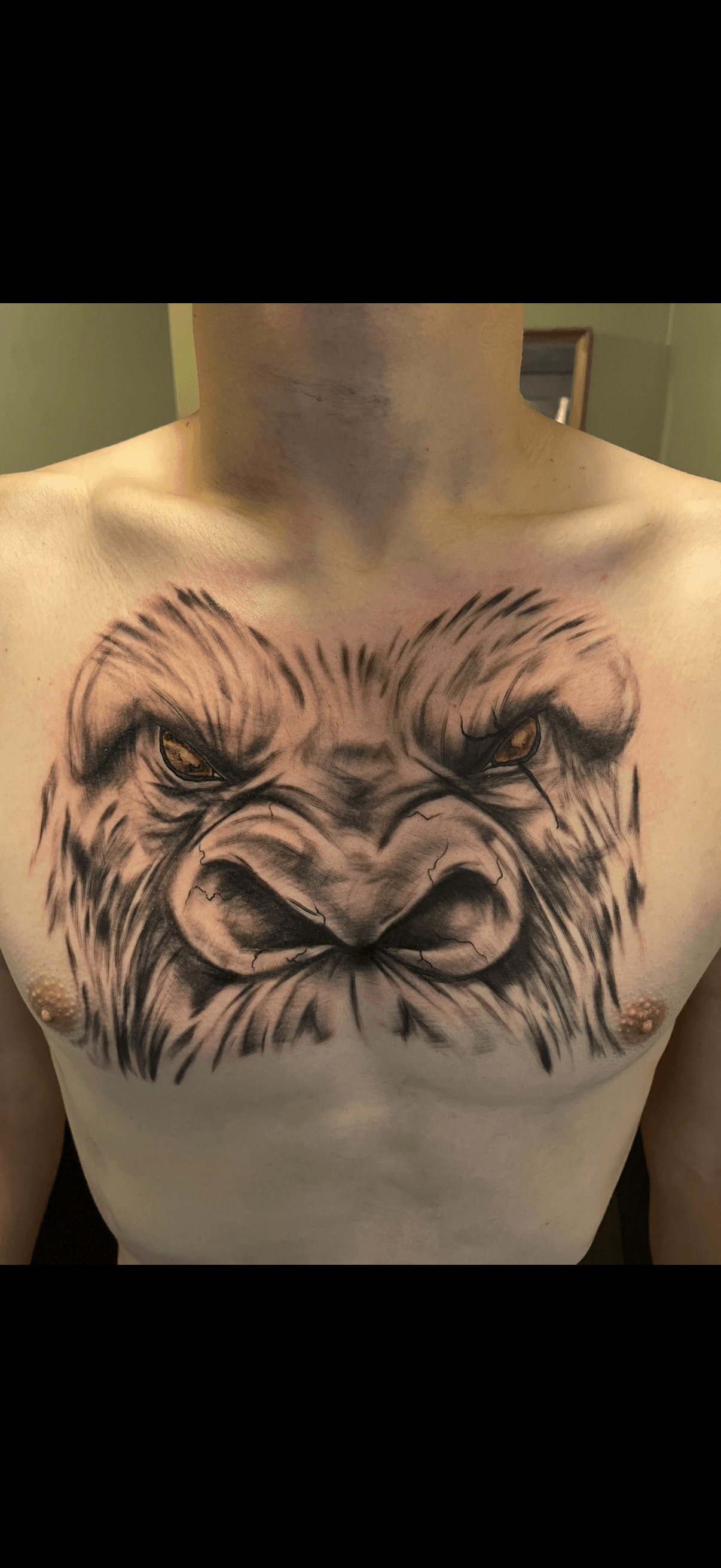 Detailed black and grey gorilla face tattoo with glowing orange eyes on a man's chest.