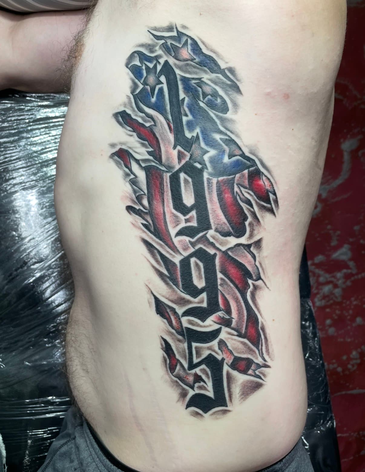 Tattoo of the year 1995 in gothic font over a torn American flag background.