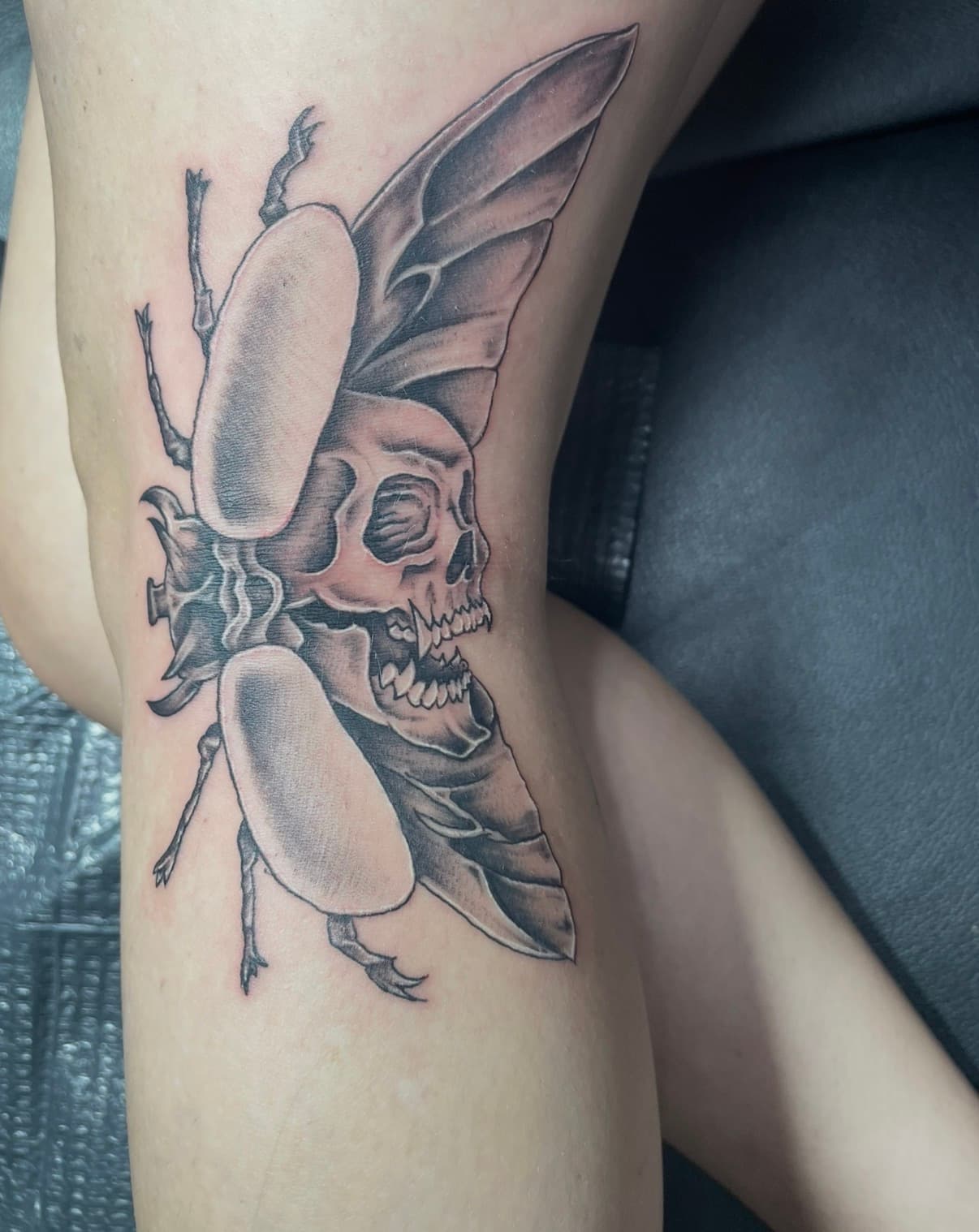 Detailed black and grey tattoo of a beetle with a human skull body and large wings.
