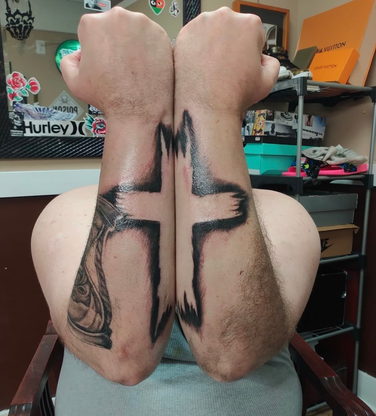 Large black brushstroke cross tattoo spanning across two forearms held together side-by-side.
